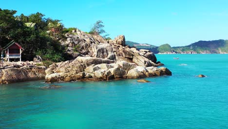 Hermosos-Acantilados-De-Piedra-Caliza-En-La-Costa-De-Una-Isla-Tropical-Bañada-Por-Tranquilas-Aguas-Azules,-Cabañas-De-Playa-Con-Vista-Al-Mar-En-Tailandia