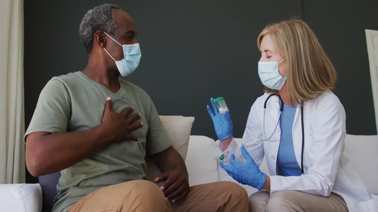 Caucasian senior female doctor holding medication talking with male patient in bed both wearing face