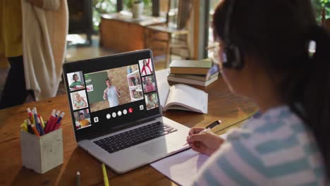 schoolgirl using laptop for online lesson at home, with diverse teacher and class on screen