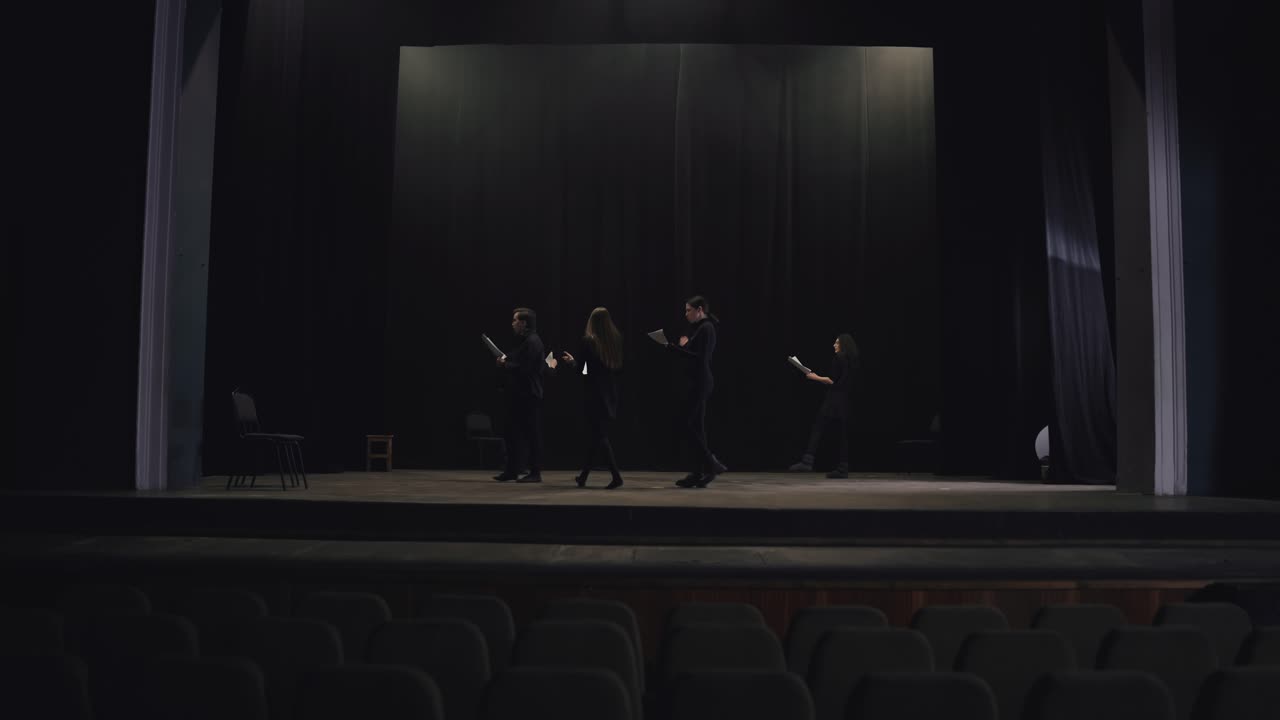 grupo confiado de jóvenes actores con trajes negros caminan en círculo en el escenario del teatro y leen sus palabras durante la preparación y el ensayo para una actuación en el teatro