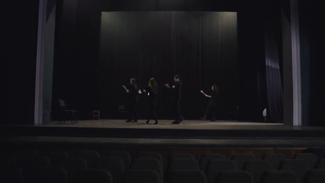 confident group of young actors in black suits walk in a circle on stage in the theater and read out their words during preparation and rehearsal for a performance in the theater