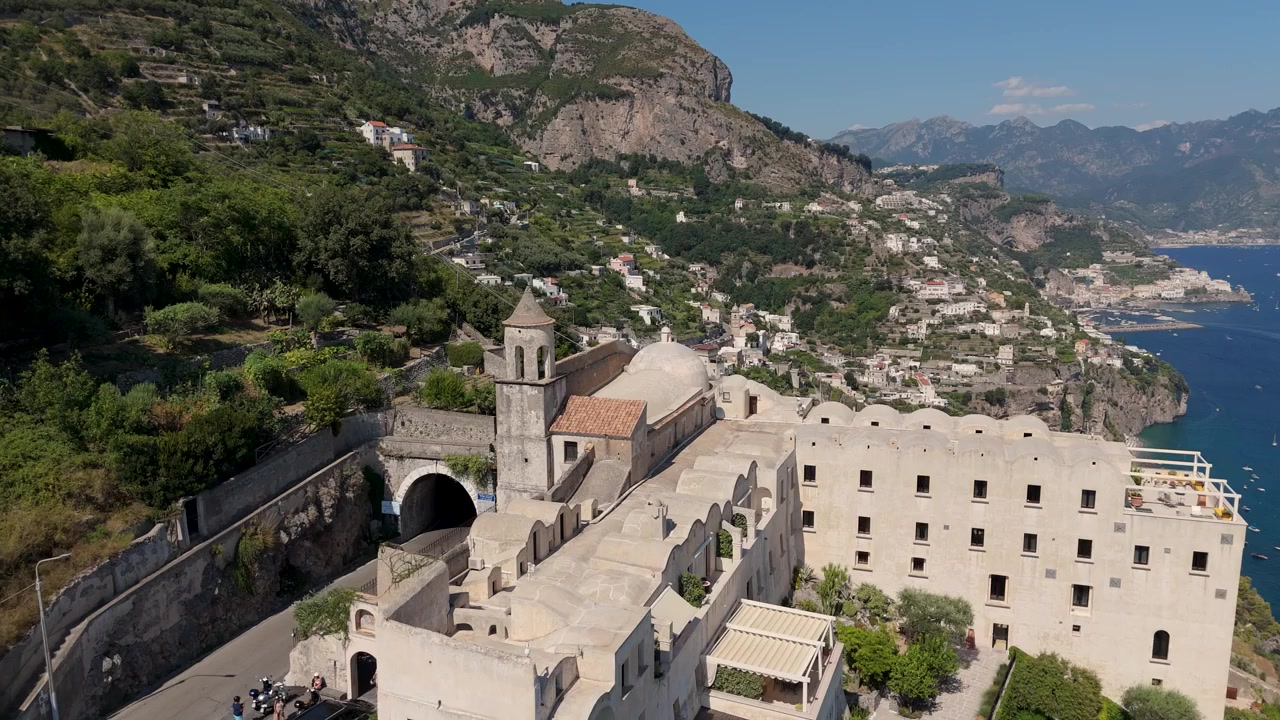 Il filmato mostra la Costiera Amalfitana con i suoi edifici unici e il mare blu sotto la luce del sole. Il video cattura la costa e le montagne vicine. Una strada attraversa l'area.