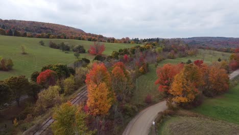 pull back autumn drone view of rail track and dirt road with colorful leaves in ontario