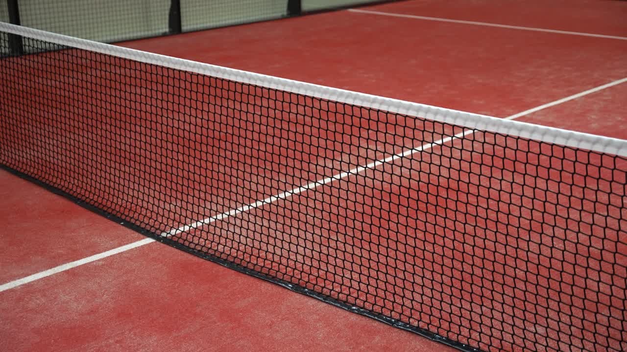 Clay padel tennis court net in focus, vibrant red surface, sporting calm
