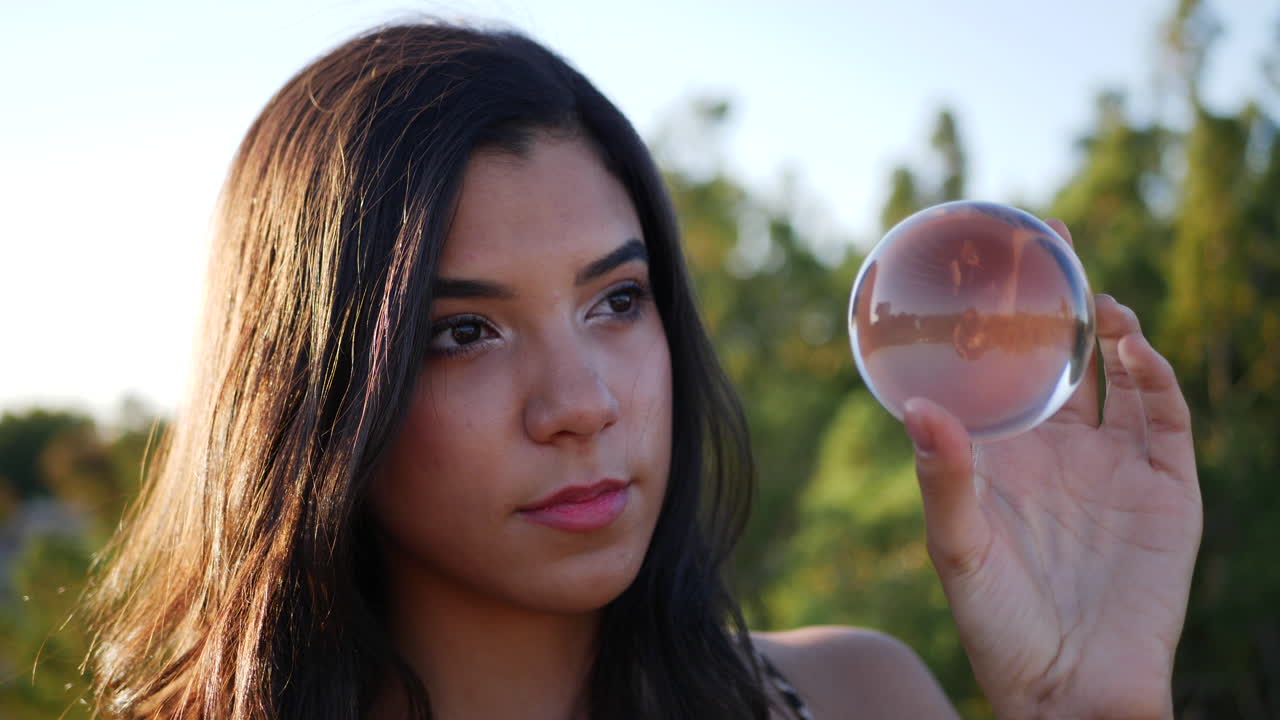 una mujer bonita en una tierra de fantasía mística lanzando un hechizo o encantamiento y mirando con ojos curiosos una bola de cristal mágica de cerca
