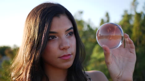 Una-Mujer-Bonita-En-Una-Tierra-De-Fantasía-Mística-Lanzando-Un-Hechizo-O-Encantamiento-Y-Mirando-Con-Ojos-Curiosos-Una-Bola-De-Cristal-Mágica-De-Cerca