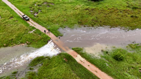 two men check if it's safe to cross flooded bridge after heavy rainfall, aerial