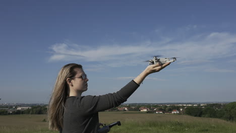 mujer joven aterrizando un dron quadcopter de consumo en su mano en un día soleado, fotograma completo a cámara lenta