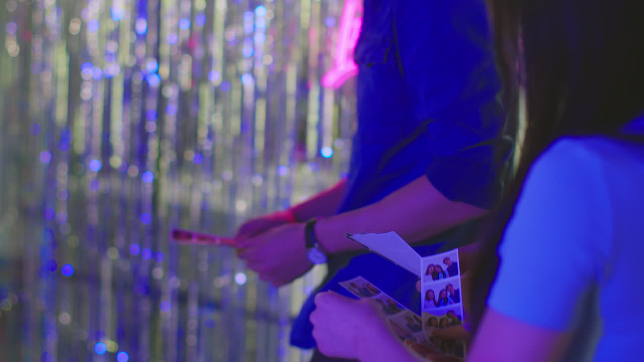 grupo de amigos divirtiéndose mirando las impresiones de la cabina de fotos en un club nocturno o feria