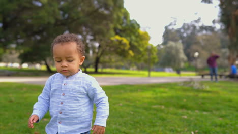 Mixed-race-boy-walking-on-grass,-waving-hand,-saying-something