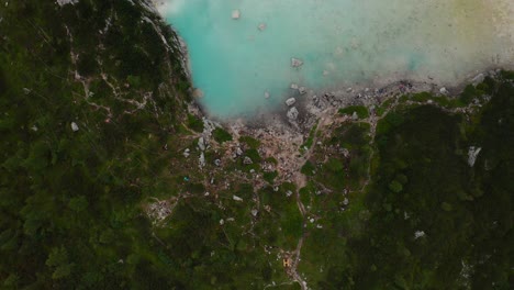 High-top-down-aerial-shot-of-lush-greenery-with-bright-turquoise-blue-water-in-Lake-Sorapis-in-Italy