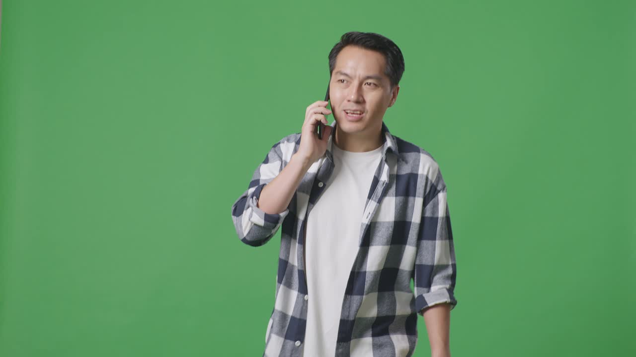 스튜디오 에서 녹색 스크린 을 걸으면서 휴대 전화 로 이야기 하는 아시아인