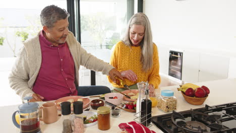 eating breakfast together, multiracial senior couple enjoying morning meal at home kitchen