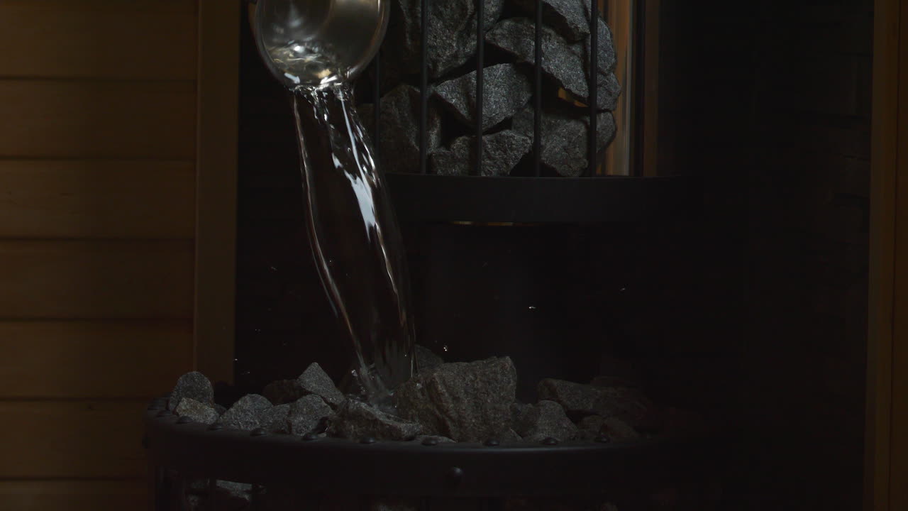 Sauna device wetting hot stones to make steam. Close up, slowmo. Static