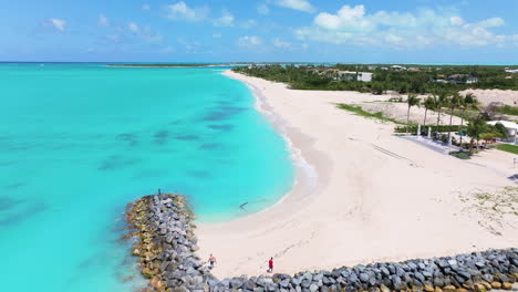 a forward medium shot of bright clear blue waters and white powdered sand with rock formation and waves gently hitting it