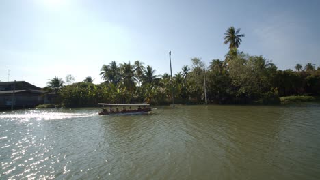 a taxi boat or ferry gliding along a calm river through a village in thailand