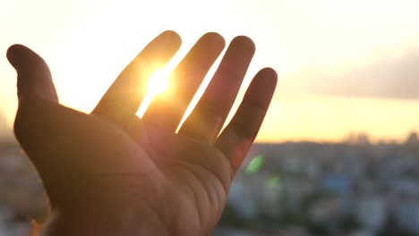 hand reaching for the setting sun over a city