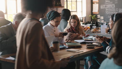 diverse business people working in cafe bustling with activity drinking coffee relaxing on lunch using technology in busy restaurant