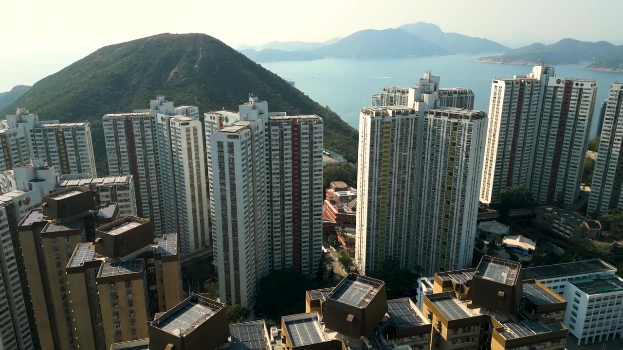 Tomada aérea de drone em ângulo alto voando sobre os arranha-céus de Hong Kong na suave luz da manhã, exibindo a densa arquitetura urbana e a escala da cidade moderna. Ideal para viagens, turismo, negócios e cinematografia urbana.