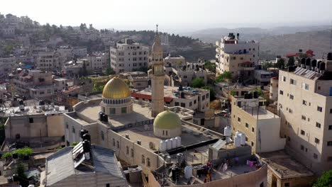 aerial view of an ancient mosque with a golden dome and minaret in a middle eastern town