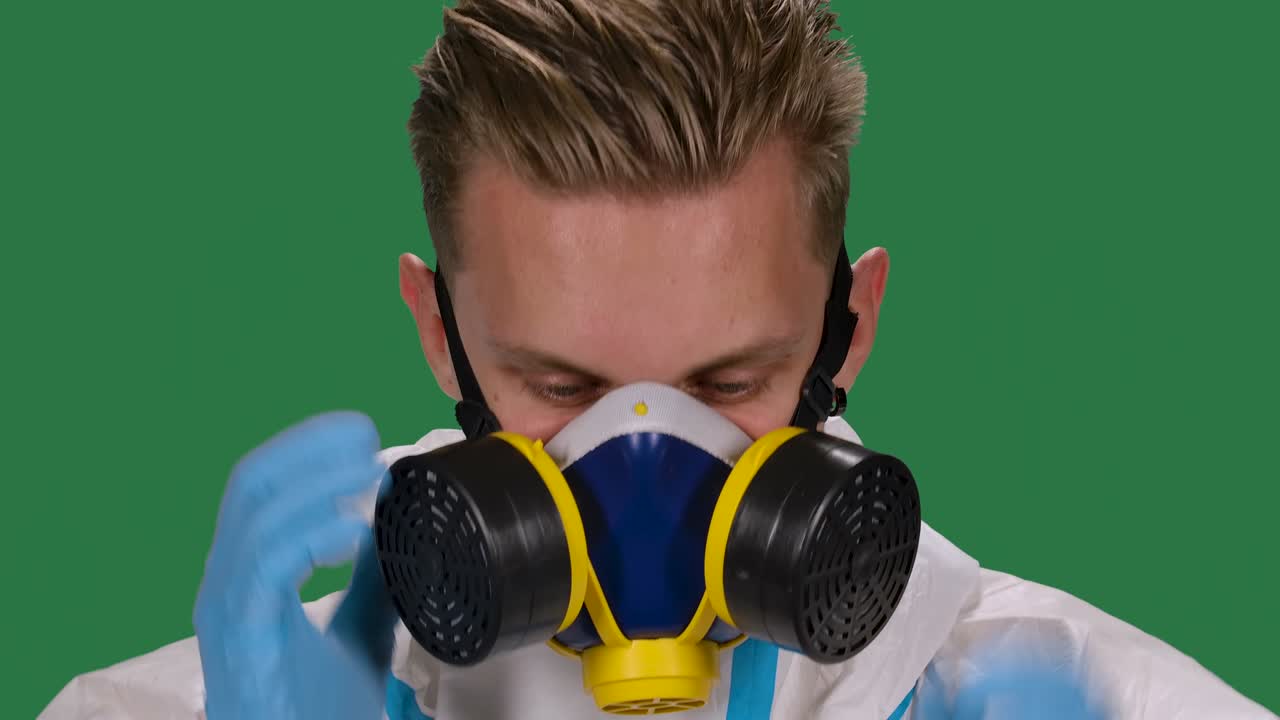 색 보호복과 수술 장갑을 입은 남성 의사의 초상화, 카메라를 바라보며 의료 호흡기와 안전 안경을 착용합니다. 녹색 스크린, 크로마 키, 느린 동작.