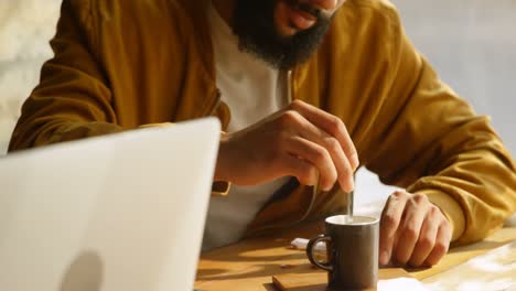 Front-view-of-young-mixed-race-man-stirring-a-cup-of-coffee-with-spoon-in-cafe-4k