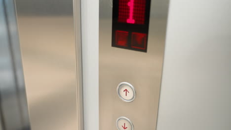 a modern elevator panel with up and down buttons. the scene shows a finger pressing the up button, highlighting the illuminated floor number display and the sleek metallic finish of the panel