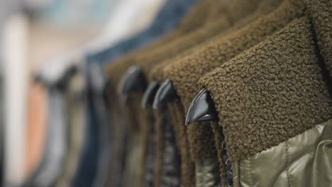 close-up of neatly arranged jackets in various earthy tones, featuring soft wool and quilted materials on sleek black hangers, emphasizing textured details, modern outerwear design