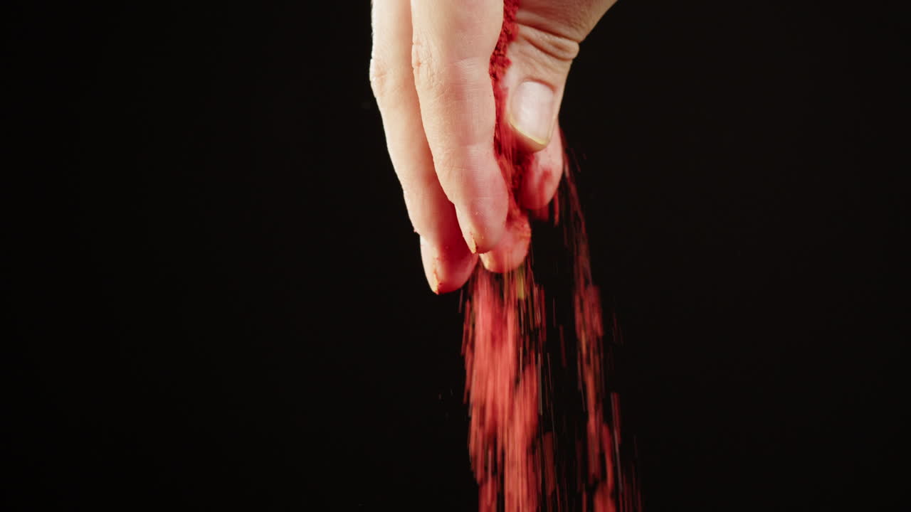 Nahaufnahme einer Hand, die rotes Pulver auf schwarzen Hintergrund streut