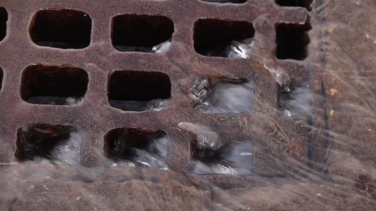 Clear rainwater running into a cast iron road drain. Autumn. UK