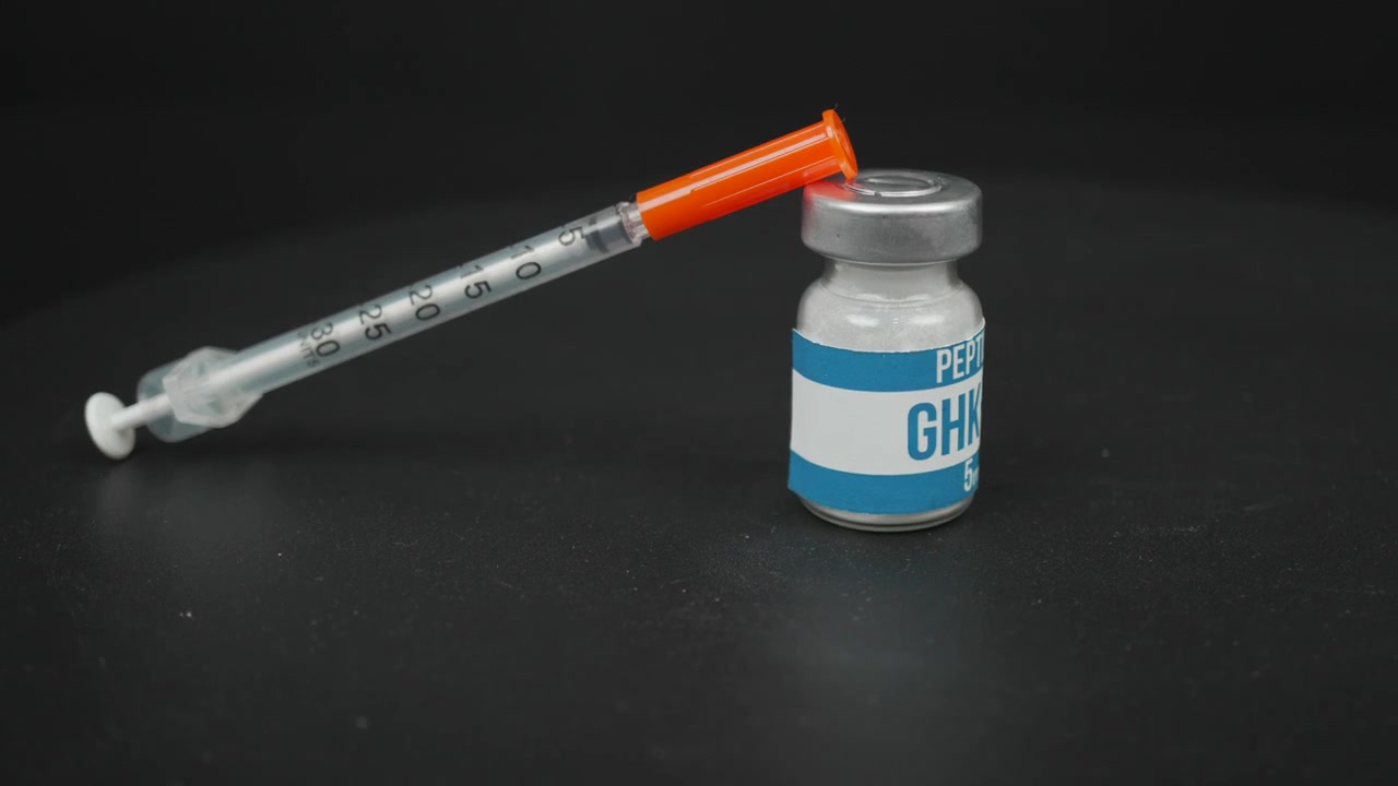Medicinsk insulinsprøjte hviler på en mærket GHK-Cu peptidflaske mod en mørk studiebaggrund, nyttig til sundheds-, bioteknologi- eller farmaceutiske temaer