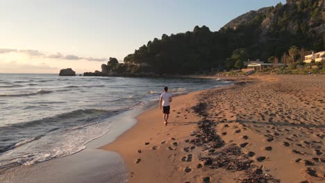 lonely man walking on an empty beach, close to the water at sunset time