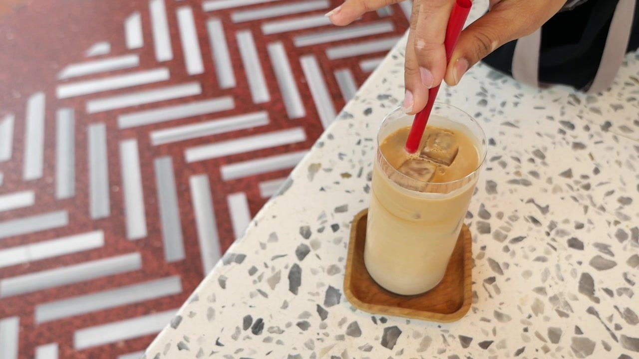Primo piano di una mano che mescola caffè freddo con una cannuccia rossa