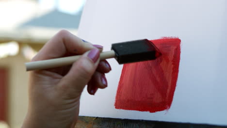 video en cámara lenta de la mano de una artista femenina usando barniz de uñas rosa aplicando pintura roja al lienzo usando un cepillo de esponja