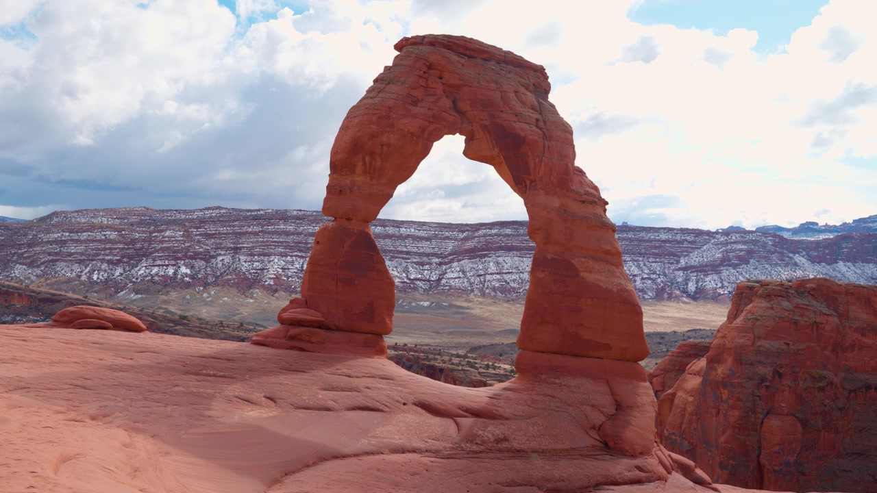 Bidikan lebar Delicate Arch di puncak pegunungan di Taman Nasional Arches saat seekor burung terbang melintas sebentar di depannya.