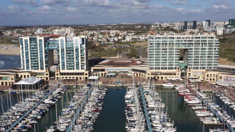 large glass hotels overlooking the long blue jetties with large side yachts and motor boats moored in the marina of herzliya in israel on a sunny day