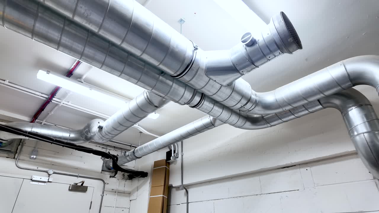 Industrial air conditioning ducts running along a building's white basement ceiling