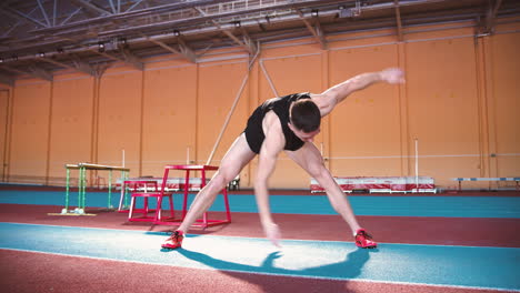 zoom in camera shot of a young sportsman doing stretch excercise and then looking at camera in indoor sport facility