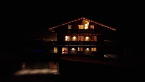 Cinematic-aerial-of-a-beautiful-chalet-at-night-in-winter-with-burning-lights