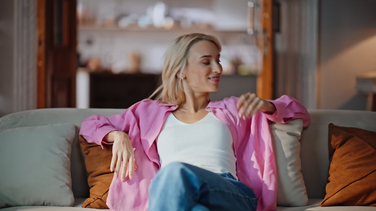 Carefree woman taking sit falling couch at home. Blonde girl looking camera