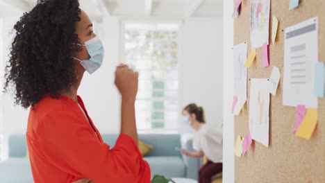 Woman-wearing-face-mask-sticking-memo-notes-at-office