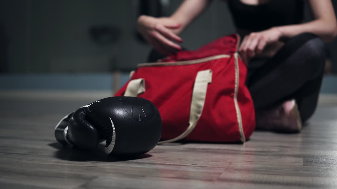 바닥에 앉아서 주머니에서 권투 장갑을 꺼내고 훈련을 준비하는 알아보기 힘든 여자. 4k로 촬영