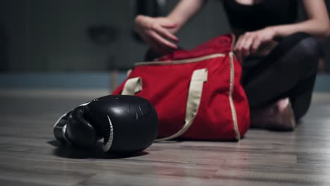 Mujer-Irreconocible-Sentada-En-El-Suelo-Y-Sacando-De-Su-Bolso-Guantes-Para-Boxeo,-Preparándose-Para-Entrenar.-Filmado-En-4k