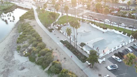 Circular-aerial-number-4-of-a-skateboard-park-during-sunset-with-young-adults-near-the-beach-and-busy-highway-in-Santa-Barbara,-California,-USA