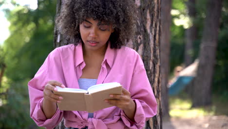 Young-black-woman-reads-a-book-in-the-woods.-Pretty-female-with-afro-hair.