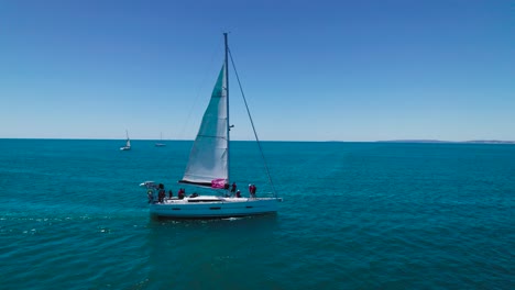 Aerial-view-of-a-white-sailboat-with-people-on-it,-in-the-mediterranean-sea