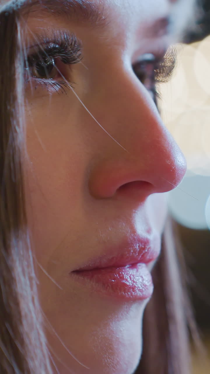 Close-up of young girl with polished nails exhaling warm breath into cold air, with visible vapor escaping, bokeh lights in background create a soft, festive atmosphere