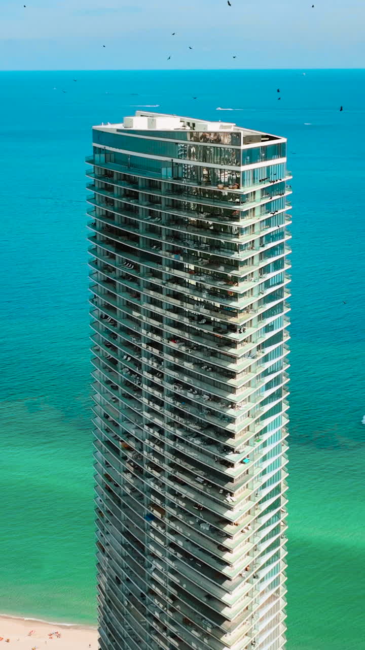 Edifícios altos de vidro de hotéis de luxo com apartamentos no plano de fundo do Oceano Atlântico. Praia de Sunny Isles em Miami. Água turquesa com barcos e ondas. Vista aérea. Vídeo vertical