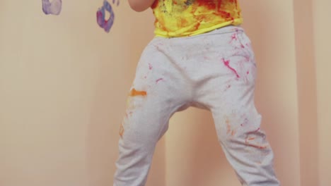 cheerful little boy is taking green color on his hands to leave handprints on the wall. slow motion