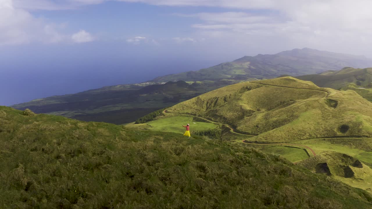 Wanita turis Asia Malaysia Tiongkok merekam video dengan ponsel di jalan setapak di tepi gunung vulkanik hijau subur, pemandangan drone di Pico da Esperança, di pulau São Jorge, Azores, Portugal